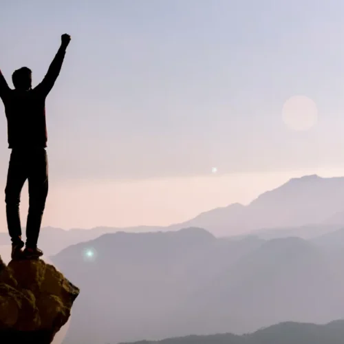 Photo of silhouetted man celebrating on mountain for "How to set goals"