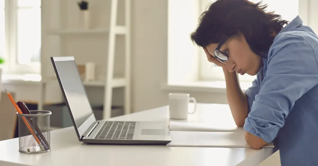 Photo of woman looking frustrated at paper and laptop for 5 mistakes you're making with affiliate marketing.